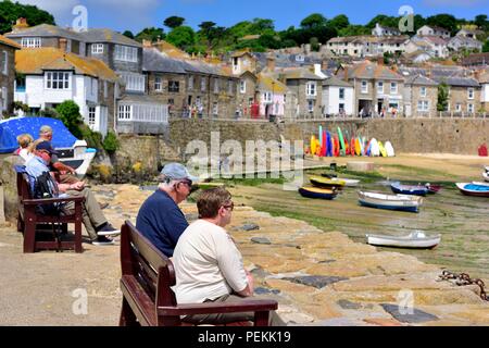 La gente seduta sulle panchine in estate sole nel villaggio di pescatori di Mousehole,Cornwall,l'Inghilterra,UK Foto Stock