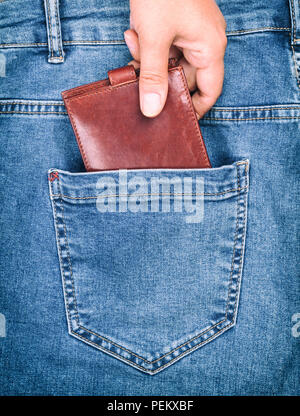 Pelle marrone portamonete risiede nella tasca posteriore dei jeans blu, una mano femminile si aggrappa a una borsa, il concetto di furto Foto Stock