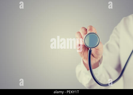 In stile retrò immagine di un medico con uno stetoscopio tenendo premuto il disco verso la telecamera in un concetto medico con un laureato sfondo grigio con copysp Foto Stock