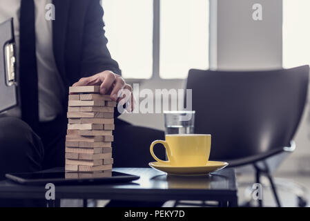 Retrò tonica immagine dell uomo d affari seduti in ufficio la costruzione di una torre di una pila di blocchi di legno in una immagine concettuale. Foto Stock