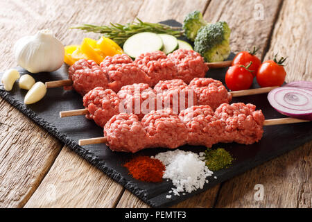 Medio Oriente Kebab da materie carni macinate su spiedini con ingredienti e verdure vicino sul tavolo orizzontale. Foto Stock