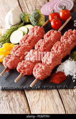 Turco kebab di greggio da carni macinate su spiedini con ingredienti e verdure vicino sul piano verticale. Foto Stock