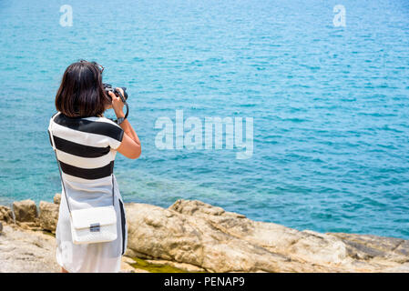 Giovane donna era felice per la fotografia con la fotocamera DSLR sulla roccia vicino al mare sotto il cielo di estate a Koh Samui Island, Surat Thani provincia, Tailandia Foto Stock