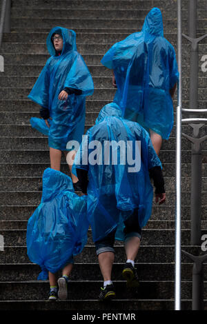 Un gruppo di persone indossano ponchos in caso di pioggia al di fuori di Wembley Park Station nel nord di Londra. Foto Stock