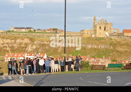 I visitatori su una condotta tour a piedi a Whitby, North Yorkshire, con la chiesa o la St Mary e Whitby Abbey in background. Foto Stock