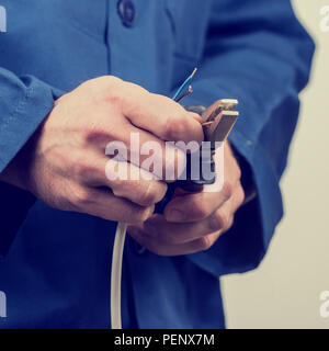 Chiudere fino alle mani di un elettricista lavorando sul cablaggio servendosi di una pinza per spellare il rivestimento plastico off le estremità, effetto retrò aspetto sbiadito. Foto Stock