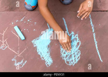 Little Boy disegno con gesso colorato sul pavimento di mattoni in estate. Foto Stock