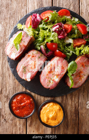 Speziato arrosto di maiale petto e fresca insalata di verdure sono serviti di ketchup e senape sul tavolo. Verticale in alto vista da sopra Foto Stock