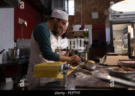 Baker preparare la pasta mentre co-lavoratore utilizzando tavoletta digitale il suo accanto a Foto Stock