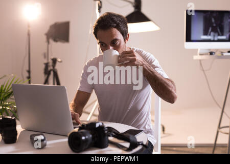 Fotografo maschio avente il caffè durante l'utilizzo di laptop Foto Stock