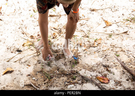 Trourist man picking up figliata possono sulla spiaggia. Foto Stock