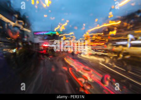 Una foto dal bus di pilotaggio in serata città durante la pioggia. Tutto è sfocato astrattamente in tracce di colori. Foto Stock