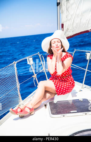 Femmina su barca a vela. Una giovane donna in un abito rosso e rosso scarpe e un cappello su uno yacht contro lo sfondo di vele e di mare Foto stock
