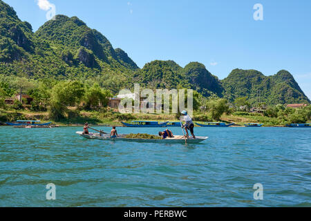 Un uomo righe una piccola canoa riempito con alghe marine in Phong Nha, il Parco nazionale del Vietnam centrosettentrionale, con montagne carsiche in background. La zona era d Foto Stock