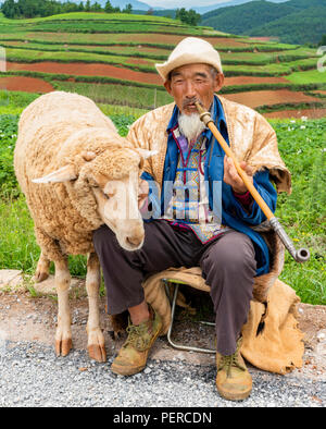Un vecchio uomo cinese vestiti con gli abiti tradizionali di fumare mentre vi godete il panorama di DongChuan nella provincia di Yunnan in Cina Foto Stock