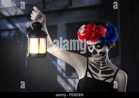 Halloween strega. Bella donna che indossa santa muerte maschera incantesimo di colata vicino alla lampadina della luce Foto Stock