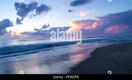 I colori pastello di uno splendido tramonto su un oceano di calma. La mattina la luce riflessa sulla superficie del mare e sulla sabbia bagnata di una spiaggia deserta. Foto Stock