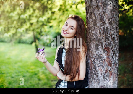 Ritratto di sorridente caucasico bianco giovane bella donna con i capelli lunghi e gli occhi castani, giocando con agitano: spinner giocattolo. Ragazza con agitano: spinner Foto Stock