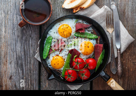 Uova fritte in padella con pomodorini, piselli verdi e pastrami. Copyspace Foto Stock