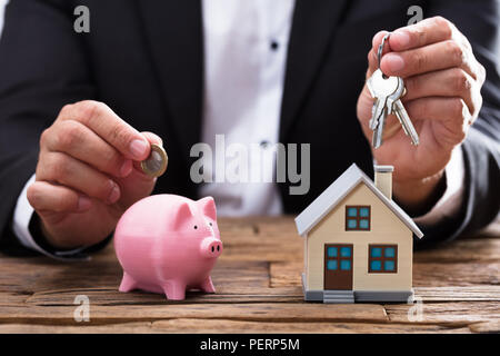 Commercianti di mano azienda moneta e chiave su piggybank e casa sulla scrivania in legno Foto Stock