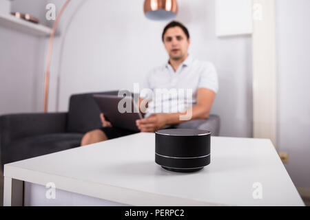 Uomo con notebook ascoltando musica su altoparlanti wireless a casa Foto Stock