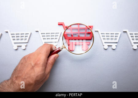 Una persona che guarda Carrello attraverso la lente di ingrandimento su sfondo grigio Foto Stock