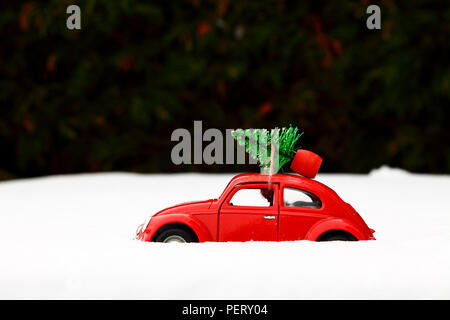 Giocattolo rossa scarabeo di Volkswagen auto con un albero di natale legata al tetto su un inverni nevosi giorno concetto di Natale Foto Stock