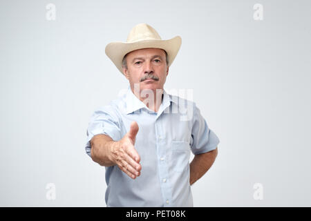 Ritratto di grave american uomo maturo nel cappello da cowboy mano di allungamento per lo scuotimento di dare il benvenuto a qualcuno o per dire ciao. Foto Stock