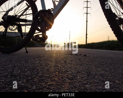 Una bicicletta parcheggiato sulla strada al tramonto Foto Stock