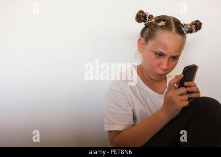 Pre-teen girl interagente con un telefono cellulare. Foto Stock