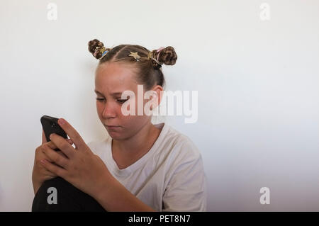Pre-teen girl interagente con un telefono cellulare. Foto Stock