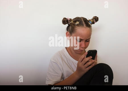 Pre-teen girl interagente con un telefono cellulare. Foto Stock