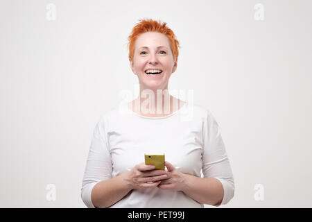 Close up ritratto di imprenditrice in t-shirt bianco e rosso di capelli corti s guardando al telefono cellulare. Ella ha ricevuto interessante offerta tramite sms Foto Stock