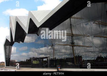 Il drammatico anteriore del Riverside Museum che si trova sulle rive del fiume Clyde. È Glasgow del museo dei trasporti ed è stato progettato da Zaha Hadid. Si tratta di un famoso museo che attira molti turisti e visitatori ogni anno. La Tall Ship, Il Glenlee, che è stato costruito sul fiume Clyde e è ormeggiata presso il museo, si riflette nelle finestre del museo. Foto Stock