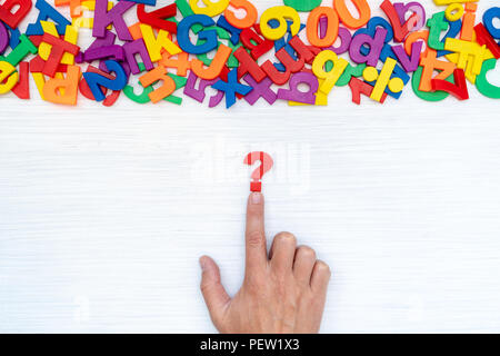 Mano con punto interrogativo sul tavolo con molti numeri di plastica e lettere. Concetto di confusione o curiosità. Foto Stock