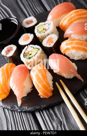 È servito un set di sushi con salmone e tonno, California rotoli maki, la salsa di soia closeup su un nero ardesia di bordo sul piano verticale. Foto Stock