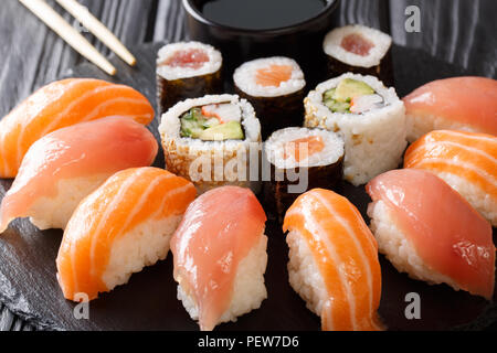Preparate di fresco sushi con salmone e tonno, California rotoli maki con la salsa di soia, bacchette di close-up sul nero ardesia scheda sul tavolo orizzontale. Foto Stock