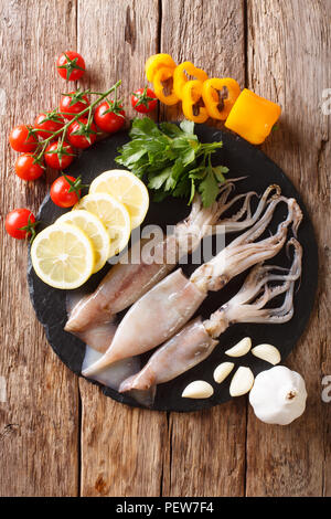 Materie calamari freschi close-up e vegetali per la cottura su una scheda di ardesia su un tavolo. Verticale in alto vista da sopra Foto Stock