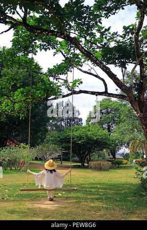 Giovane donna con cappello di paglia relax su una oscillazione di legno in giardino Foto Stock
