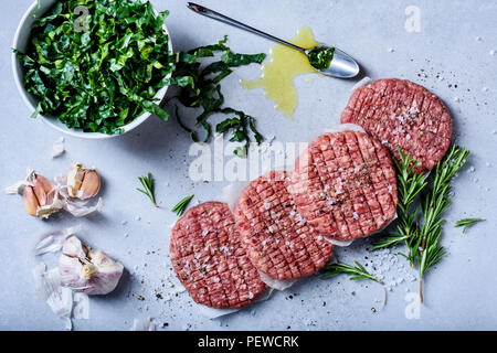 Raw hamburger di manzo polpette con insalata, erbe aromatiche e spezie, cucina salutare, grigio sfondo concreto Foto Stock