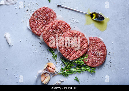 Materie organiche polpette di carne macinata per produrre hamburger di pollo con rosmarino, specie sulla tabella grigia, vista al di sopra Foto Stock