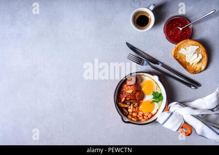 Prima colazione inglese in un recipiente di cottura con uova fritte, salsicce, fagioli, pane tostato e caffè sul tavolo in cemento, spazio di copia Foto Stock