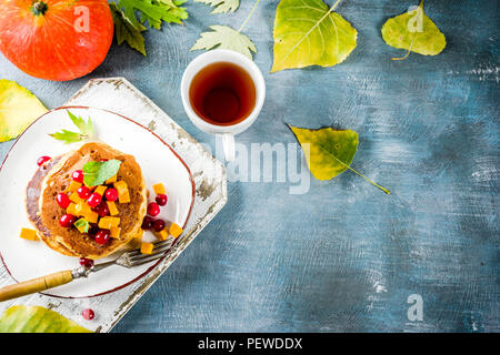 Colazione autunnali idea, Frittelle di zucca, con fette di zucca, sciroppo di acero o miele, cranberry, su un blu sullo sfondo di calcestruzzo, spazio per il testo Foto Stock