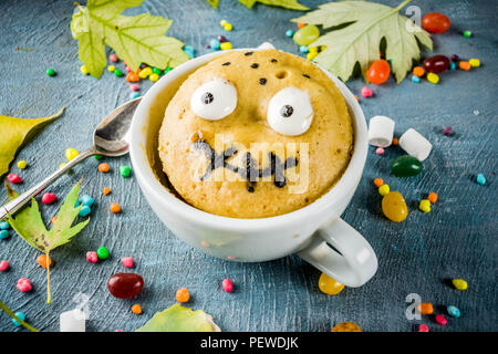 Kids Halloween idea alimentare, funny mug decorare la torta come mostro faccia con marshmallow gli occhi e la bocca dipinta con marcatore commestibili, sfondo blu con s Foto Stock