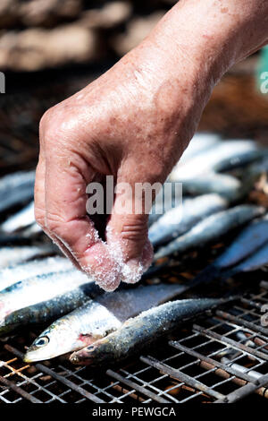 Primo piano di una vecchia donna caucasica salatura alcune materie di sardine in un grill all'aperto Foto Stock