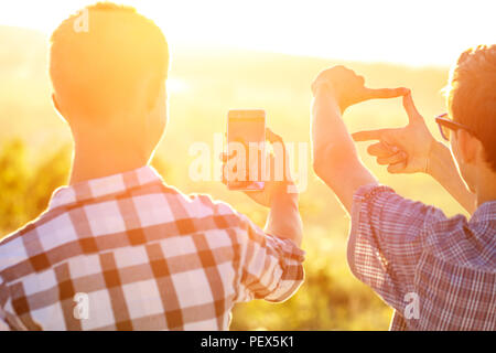 Due uomini di scattare foto del tramonto sul telefono al sole Foto Stock