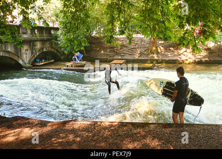 Monaco di Baviera, Germania - 24 luglio 2018 - Monaco di Baviera, surfisti in muta di pratica su onde artificiali sul Eisbach, piccolo fiume attraverso l'Englischer Ga Foto Stock