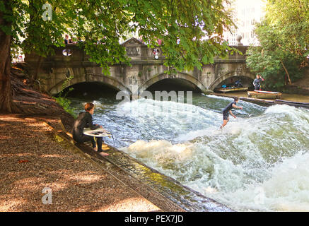 Monaco di Baviera, Germania - 24 luglio 2018 - Monaco di Baviera, surfisti in muta di pratica su onde artificiali sul Eisbach, piccolo fiume attraverso l'Englischer G Foto Stock