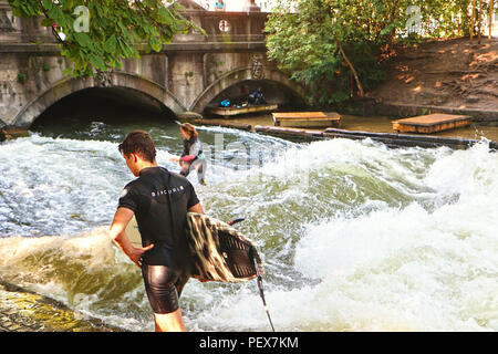 Monaco di Baviera, Germania - 24 luglio 2018 - Monaco di Baviera, ragazza nella muta Cavalca le onde artificiali sul Eisbach, piccolo fiume attraverso l'Englischer Garten, WH Foto Stock