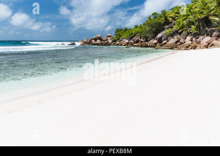 La bellissima spiaggia di sabbia bianca di Anse Cocos di La Digue, Seicelle con acqua turchese, cielo blu e verde di alberi di palma. Foto Stock